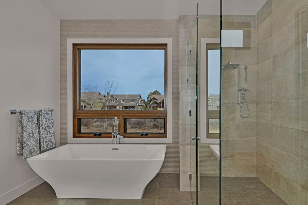 Modern bathroom with freestanding tub, large window, and tiled glass-enclosed shower.
