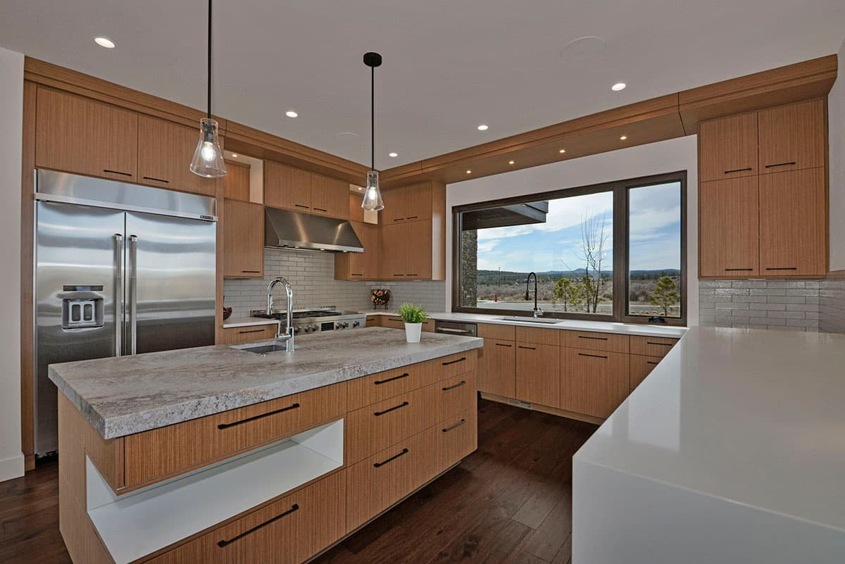 Modern kitchen with wood cabinetry, large island with sink, stainless steel appliances, and wide view window.