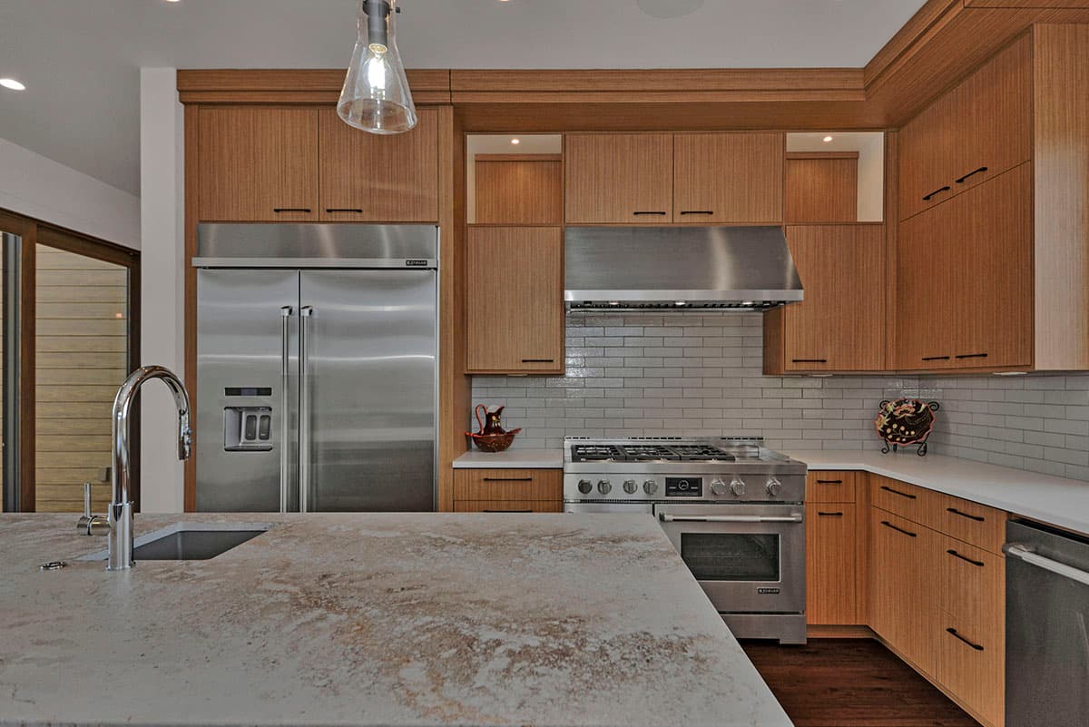 Modern kitchen with stainless steel appliances, wood cabinetry, subway tile backsplash, and island with sink.