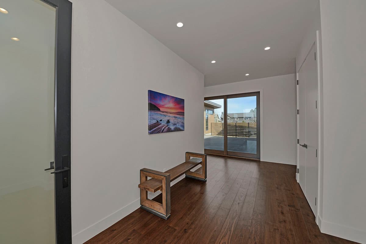 Hallway with dark wood floors, modern bench, large glass doors to patio, and contemporary art.