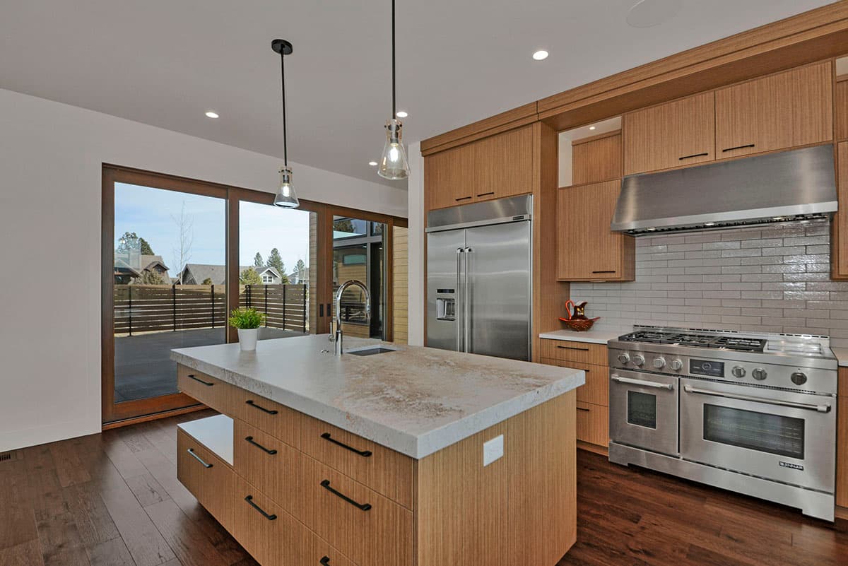 Kitchen interior with large island, stainless steel appliances, wood cabinetry, and sliding glass doors to an outdoor patio.