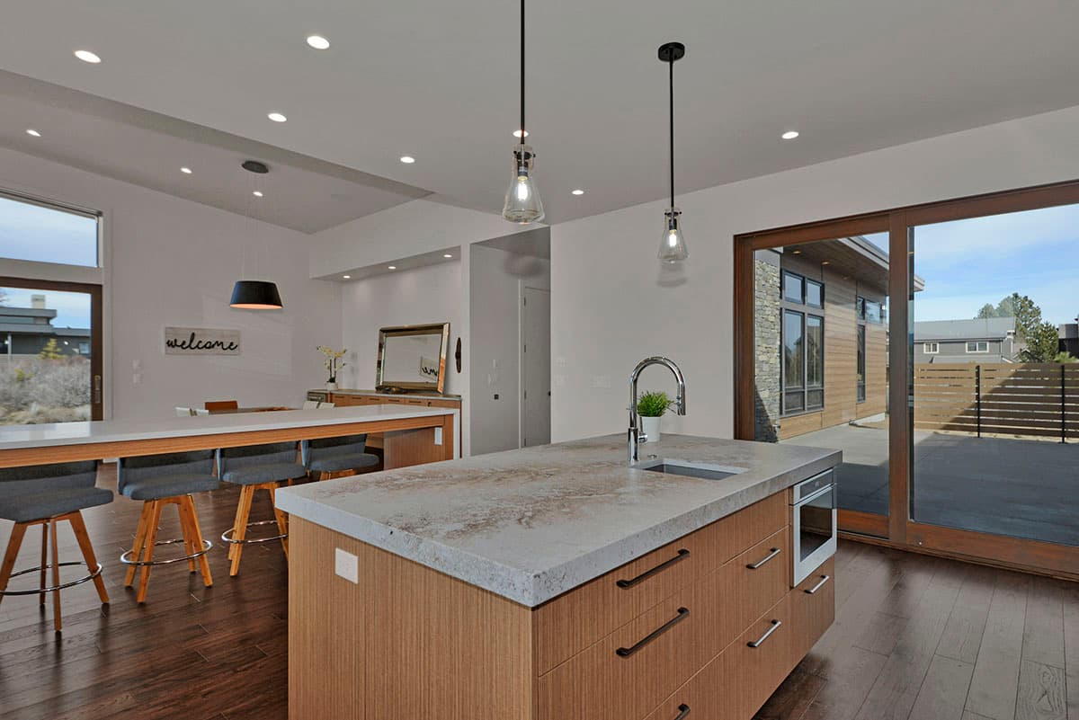Modern kitchen with island sink, light wood cabinets, and open dining area with large windows. View of patio access.