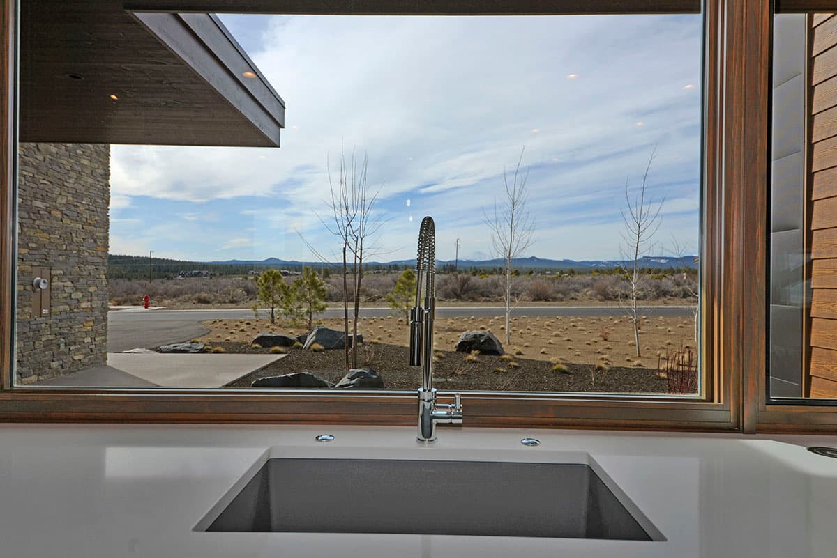 Kitchen sink view through large window with stone exterior and modern wood siding.