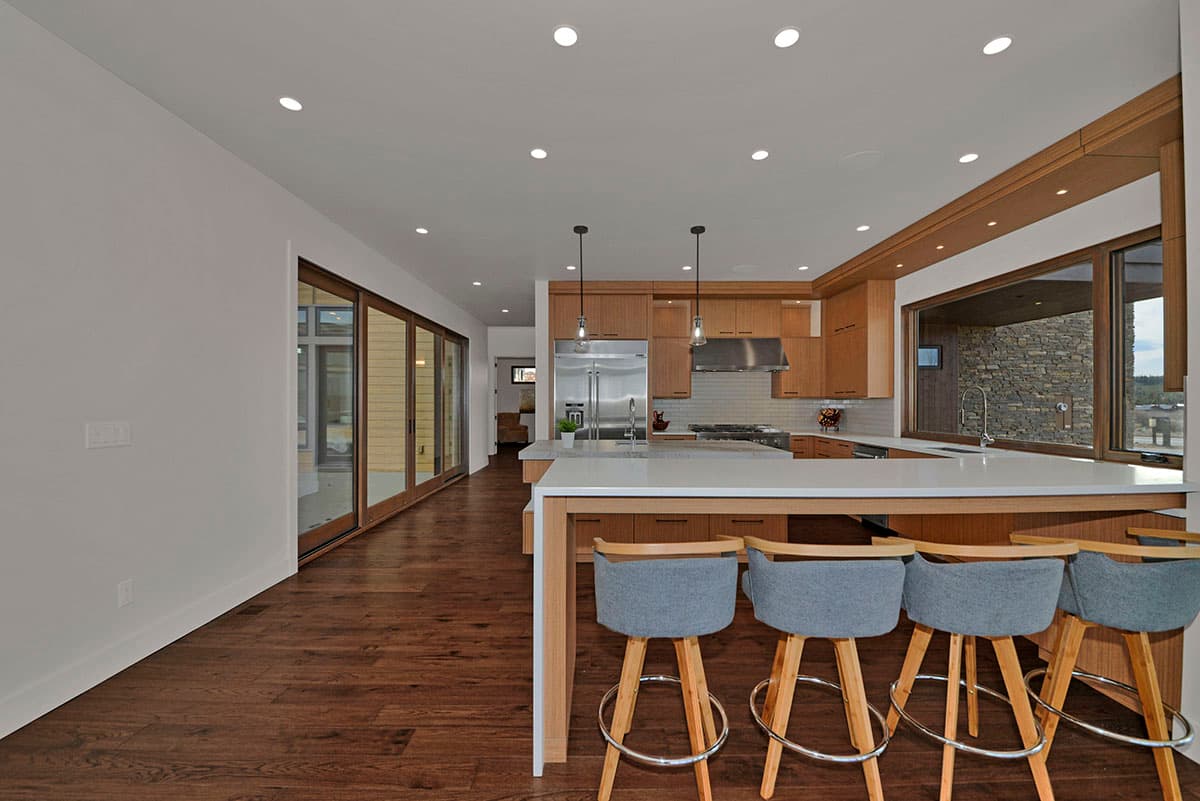 Modern kitchen with wood cabinetry, stainless steel appliances, large island with seating, and a wide picture window overlooking a stone exterior.