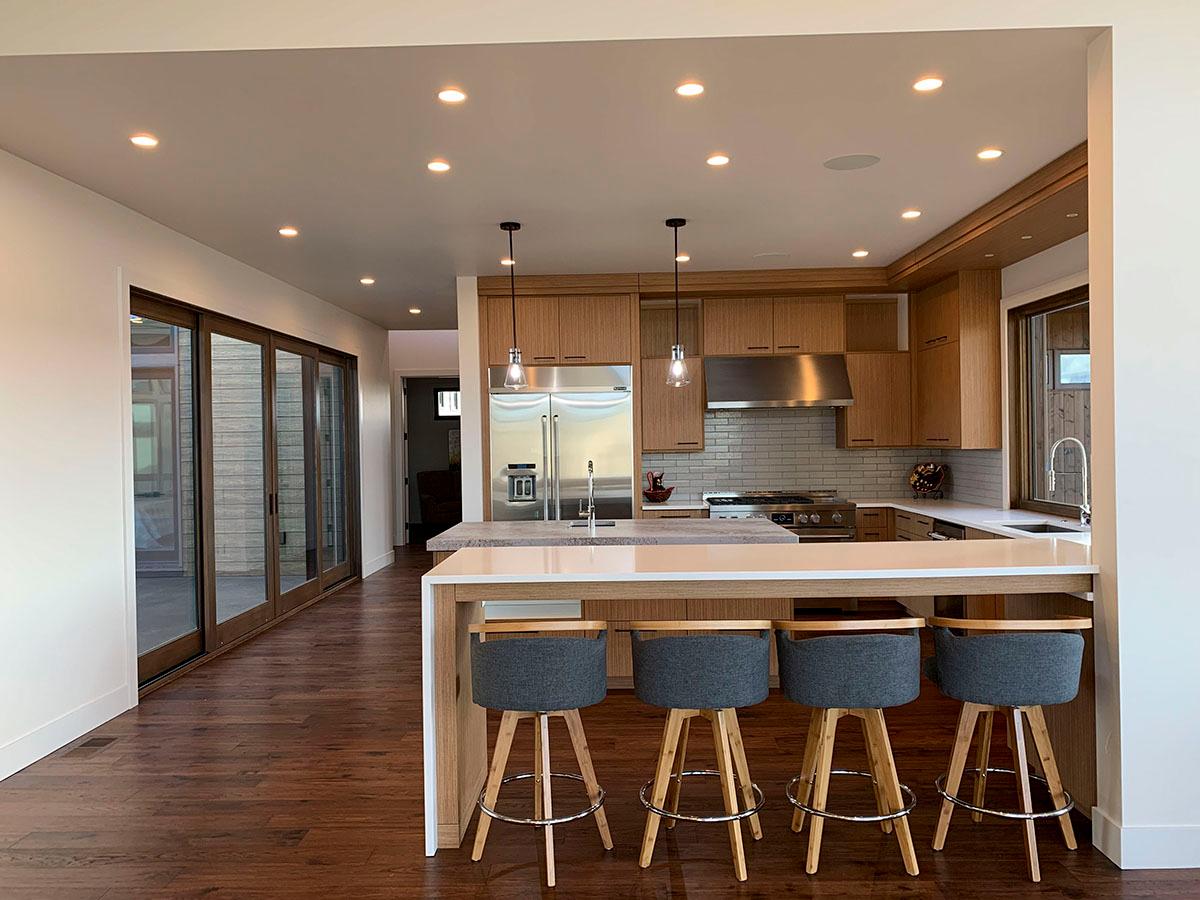 Modern kitchen with wood cabinetry, stainless steel appliances, subway tile backsplash, island with seating, and large sliding glass doors.