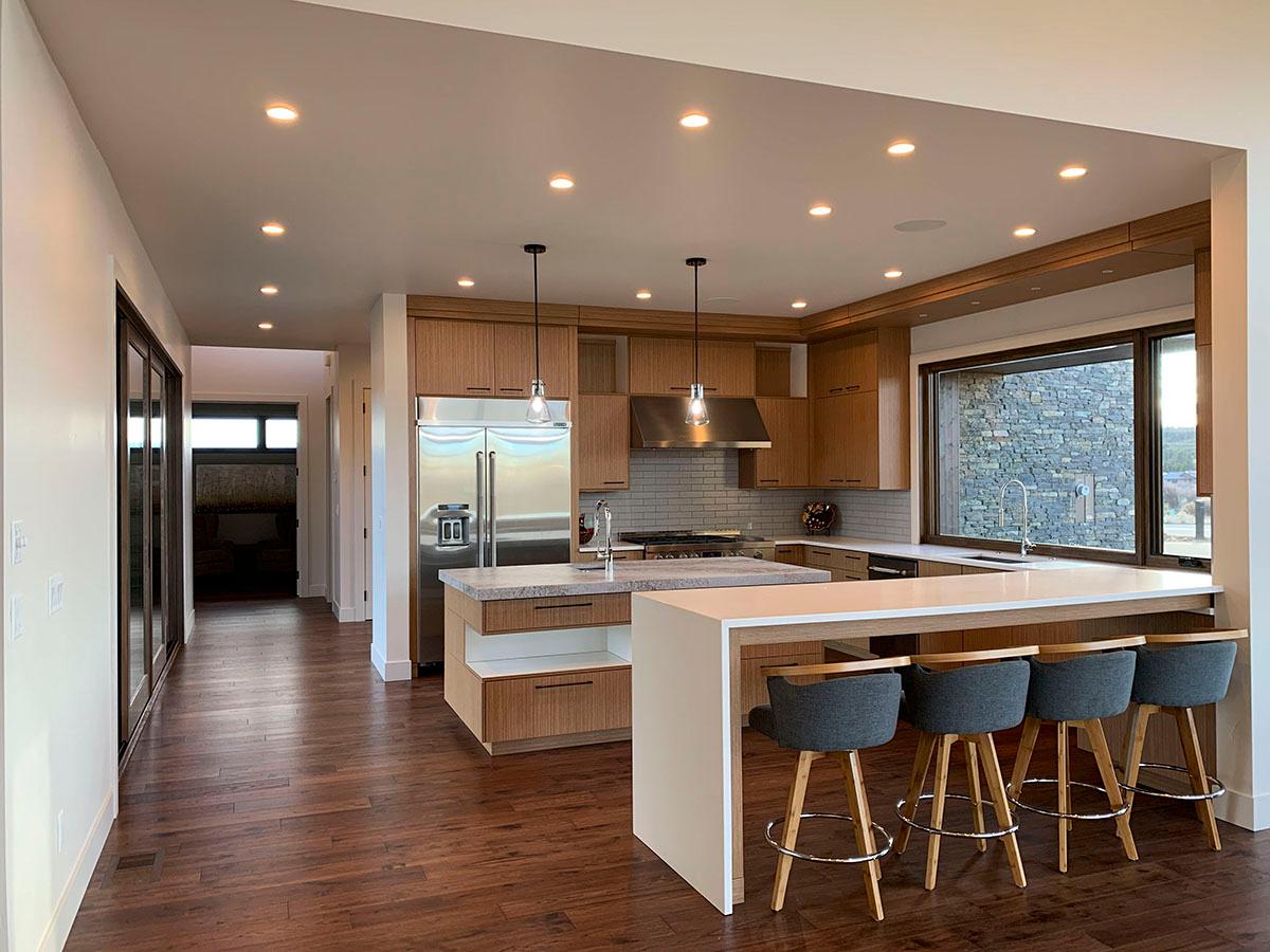 Contemporary kitchen with wood cabinetry, large island with seating, stainless steel appliances, and a wide picture window with stone exterior view.