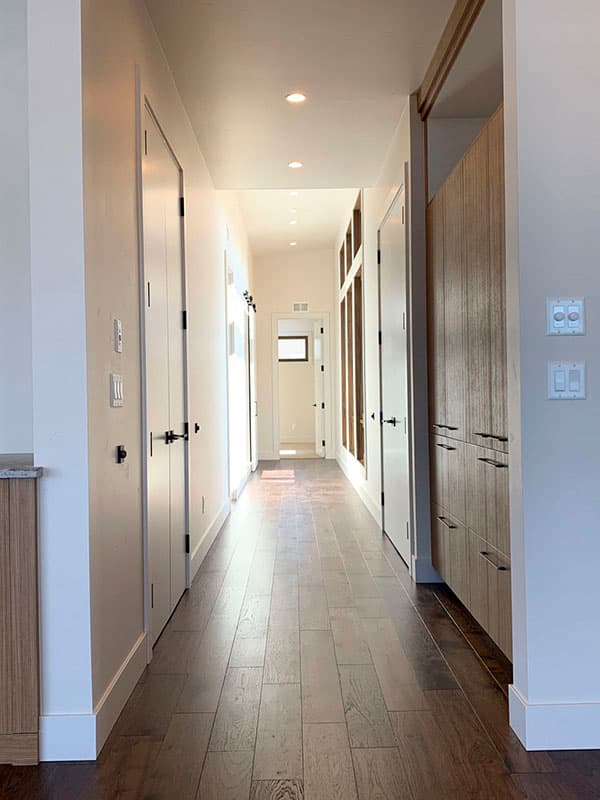 Hallway with wood plank flooring, recessed lighting, multiple doors, and wood-paneled cabinetry.