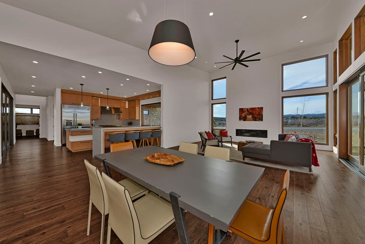 Modern open-concept living area with dining, kitchen, and fireplace. Large windows offer scenic views.