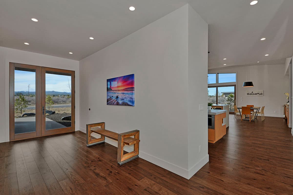 Interior view showing entry, kitchen island, and dining area with large windows and hardwood floors.