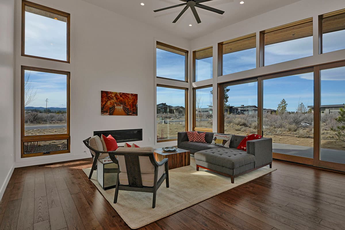 Modern living room with floor-to-ceiling windows, fireplace, sectional sofa, and wood floors.