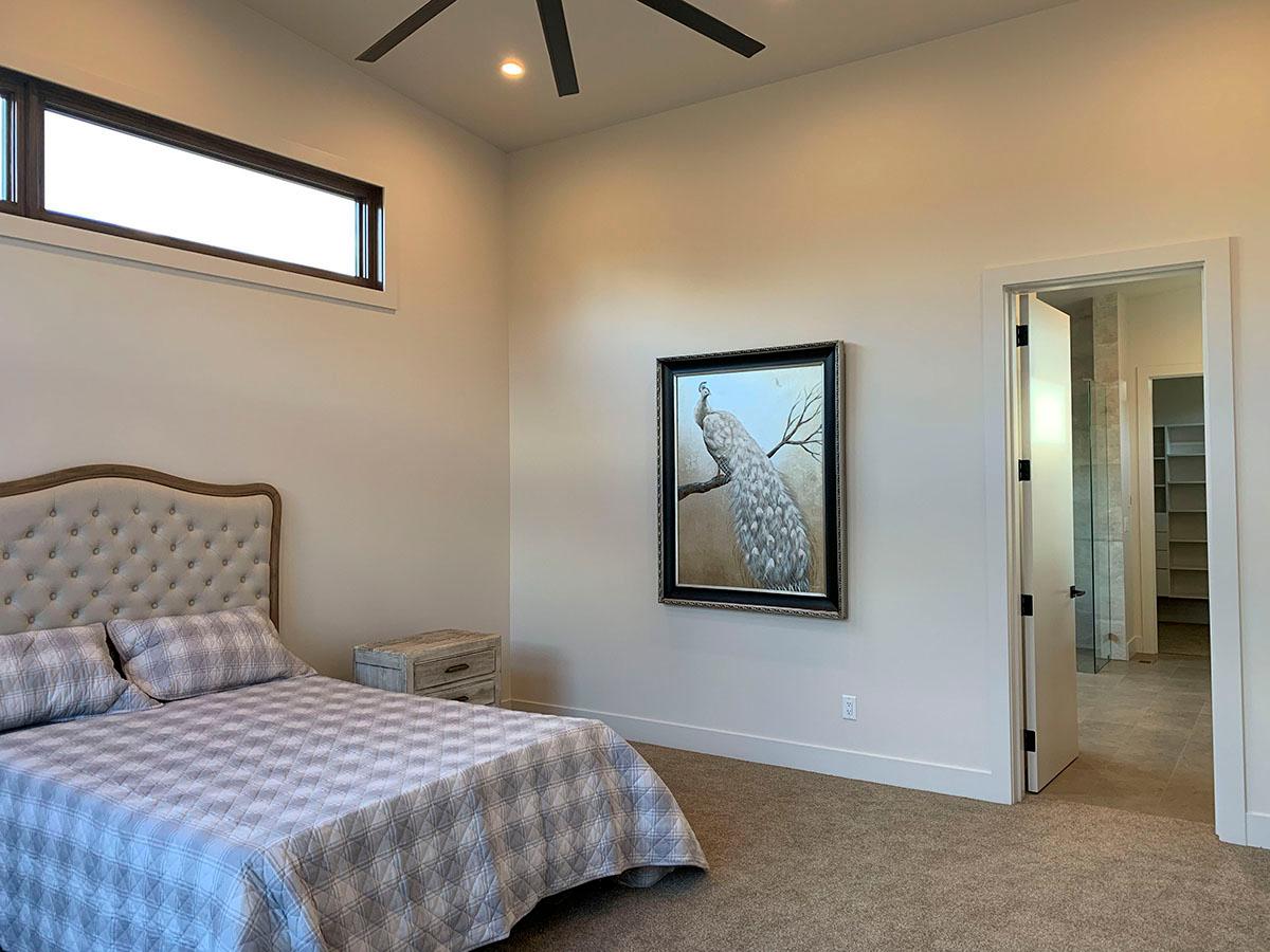 Bedroom with a tufted headboard, framed peacock art, and view into an en-suite bathroom with closet.