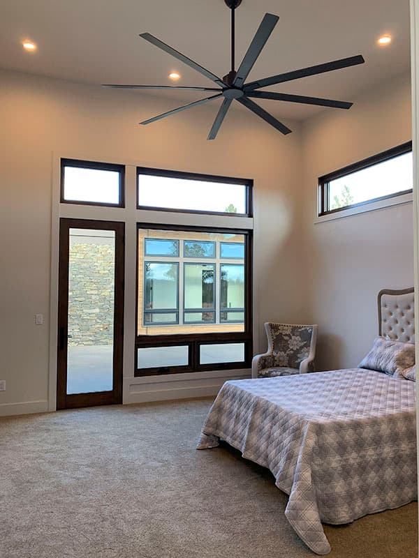 Primary suite with vaulted ceiling, large windows, ceiling fan, and door to exterior patio.