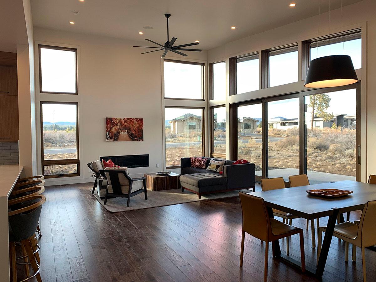 Great room with a linear fireplace, sectional sofa, and dining table with chairs. Floor-to-ceiling windows showcase the exterior landscape.