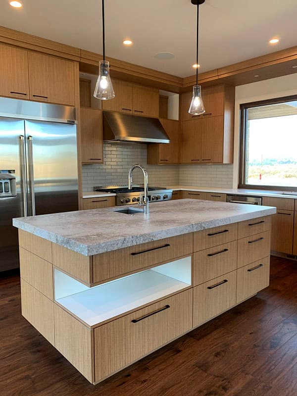 Modern kitchen with light wood cabinetry, stainless steel appliances, large island with stone countertop, and subway tile backsplash.