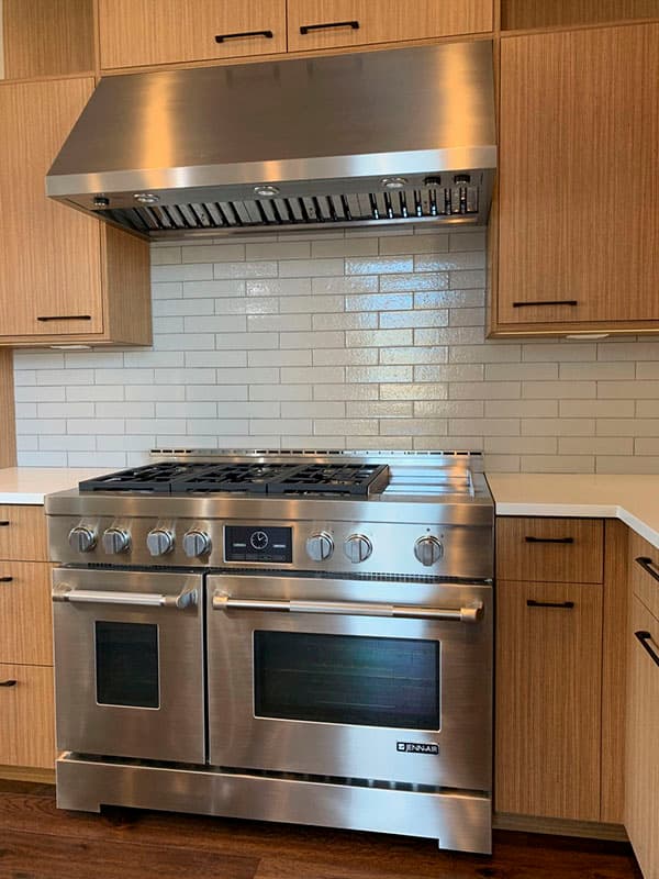 Kitchen features stainless steel professional range, subway tile backsplash, and wood cabinetry.
