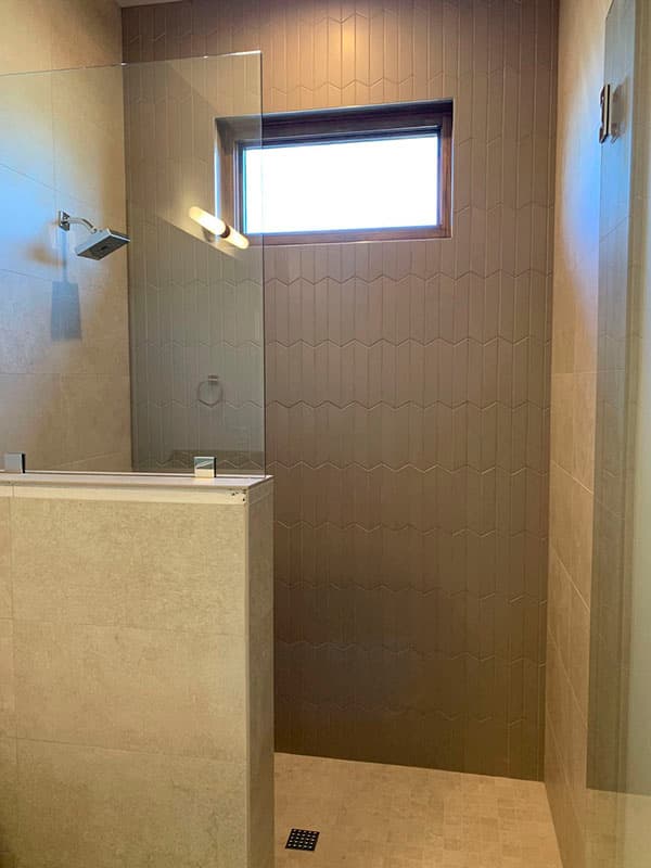 Interior bathroom featuring a glass-enclosed shower with a rain showerhead, textured tile accent wall, and a small horizontal window.
