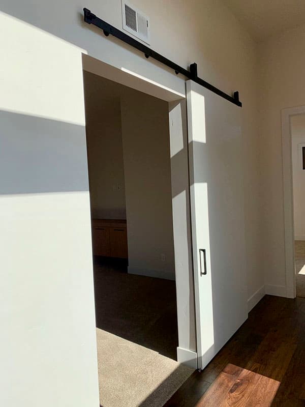 Interior view of a room featuring a modern white barn door with black hardware and a vent above.