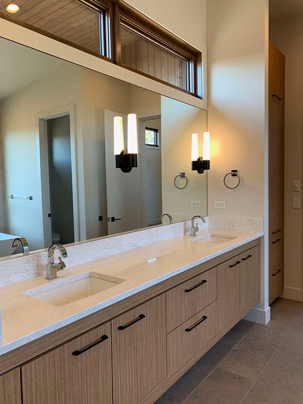 Modern bathroom with double vanity, quartz countertop, integrated sinks, wood cabinetry, sconce lighting, and horizontal clerestory windows.