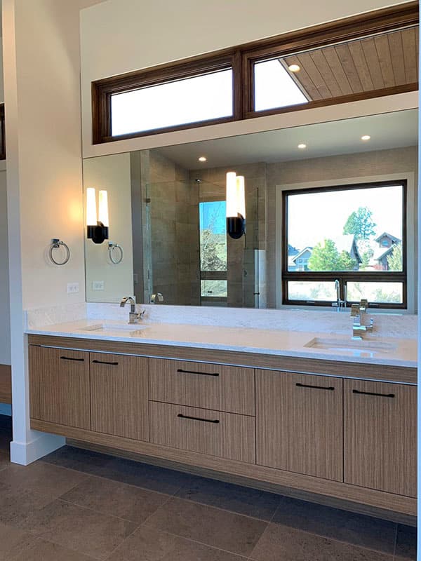 Modern bathroom vanity with wood-grain cabinets, marble countertop, dual sinks, and sconce lighting.