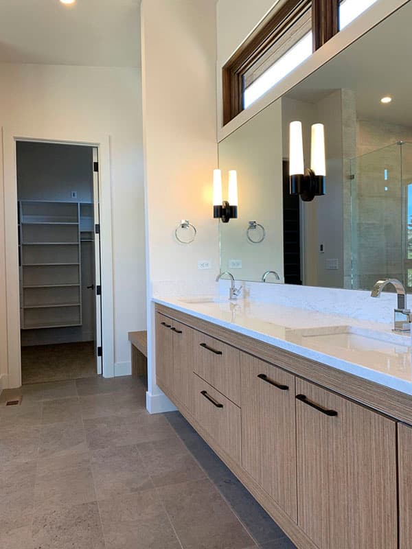 Modern bathroom with double vanity, wood cabinetry, stone tile floor, and walk-in closet.