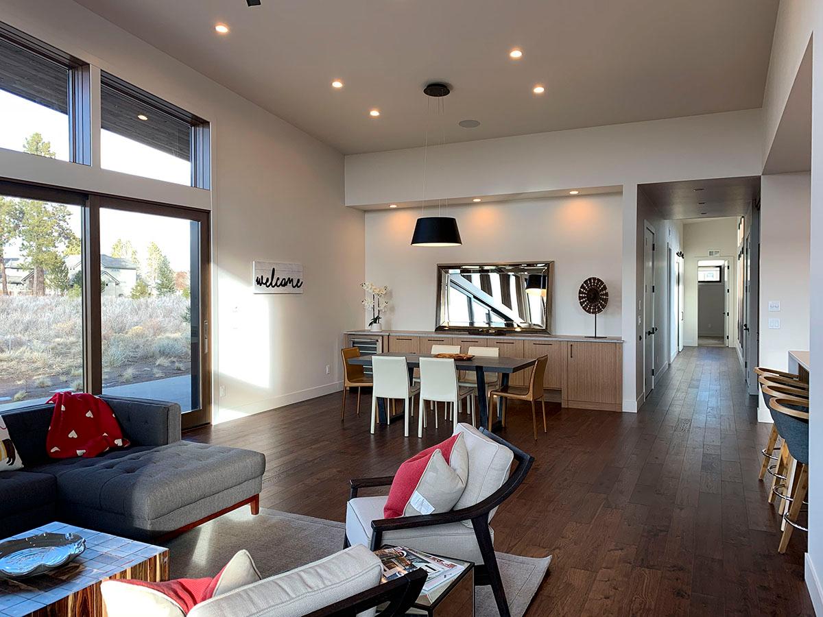 Modern open-plan living space with large windows, dining area, and hallway leading to front entrance.