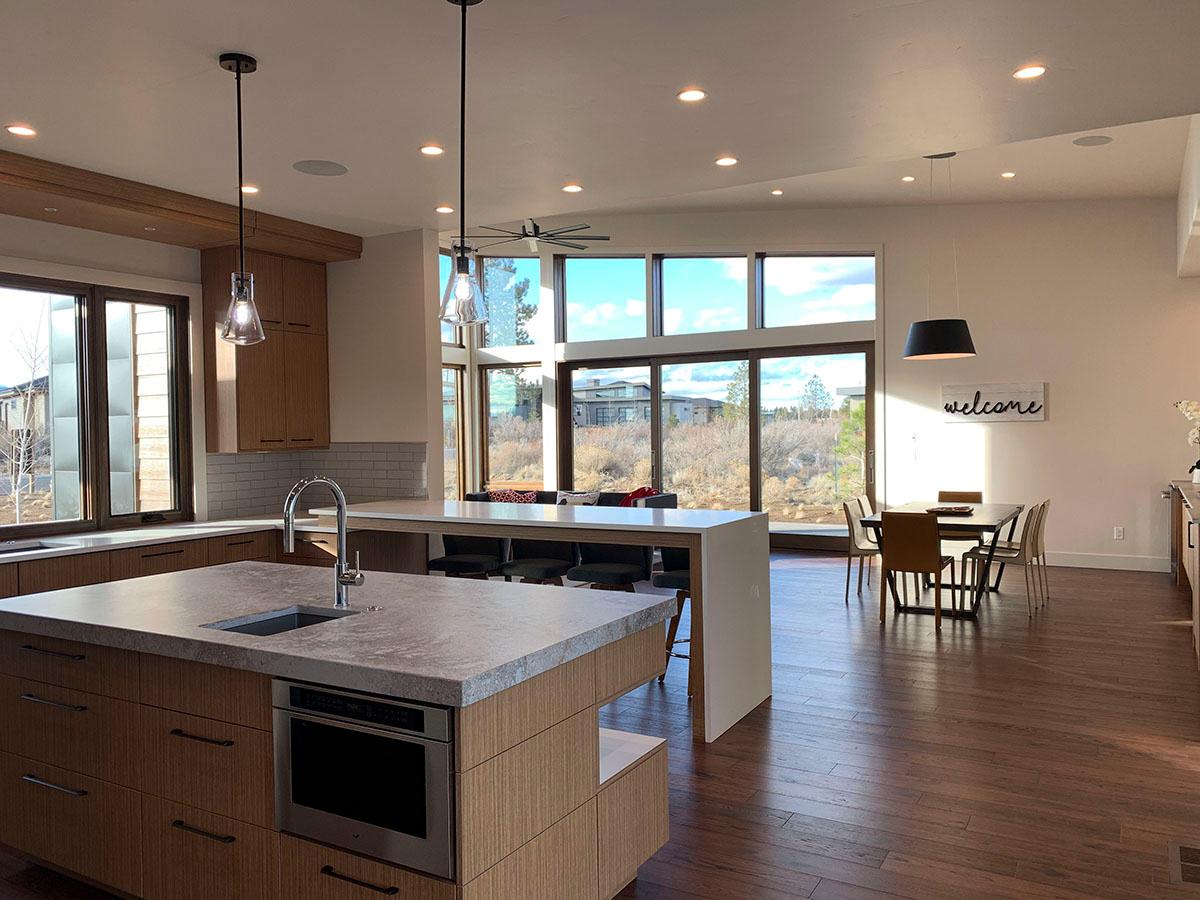 Modern open-concept kitchen with large island, dining area, and expansive windows overlooking a dry landscape.