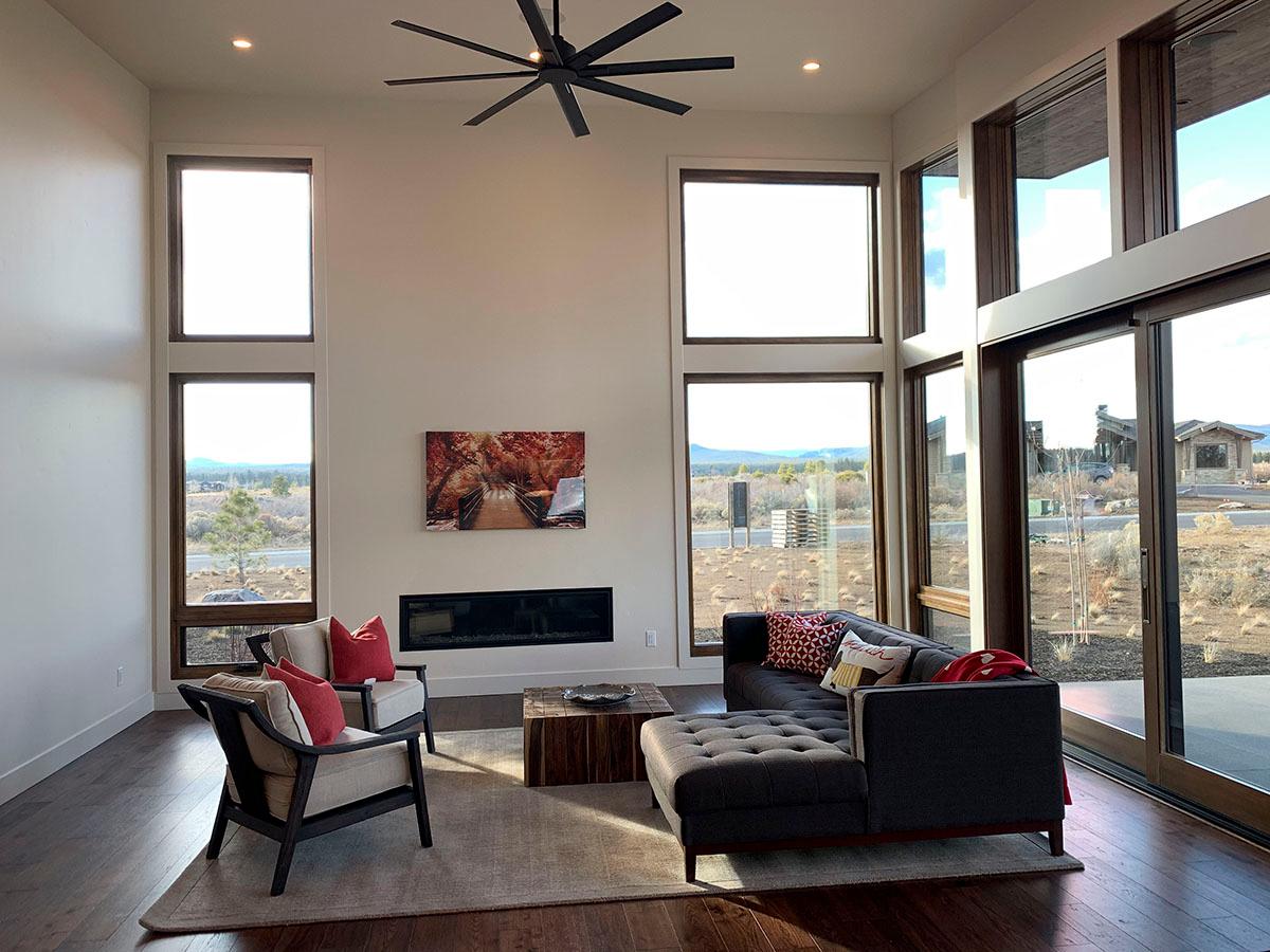 Modern living room with fireplace, floor-to-ceiling windows, sloped ceiling, and black ceiling fan.