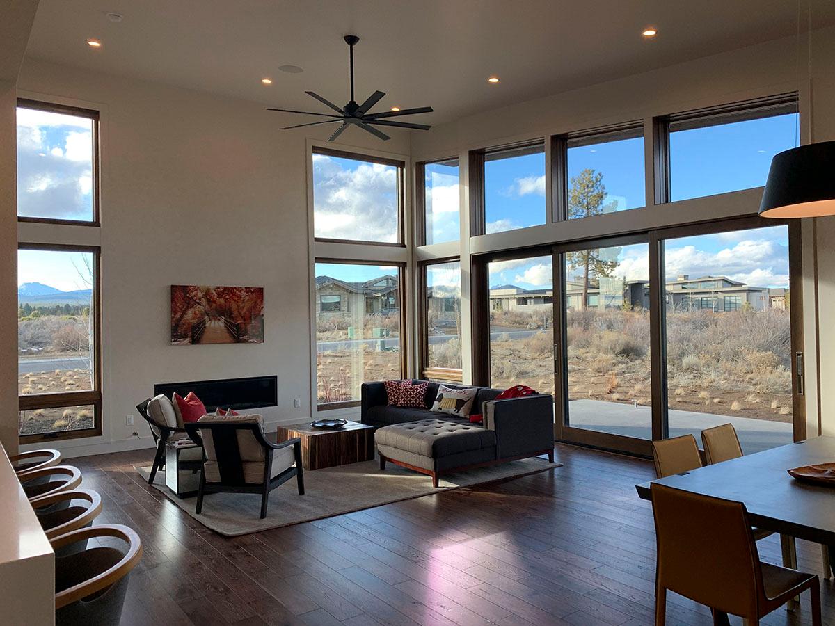 Interior view of open living area with vaulted ceiling, fireplace, and large windows overlooking outdoor landscape.