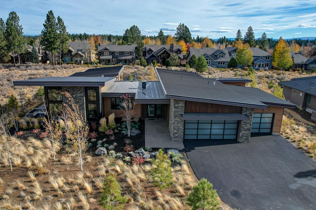 Modern house plan exterior with low-slung profile, asymmetric gables, stone and wood facade, and glass panel garage doors.