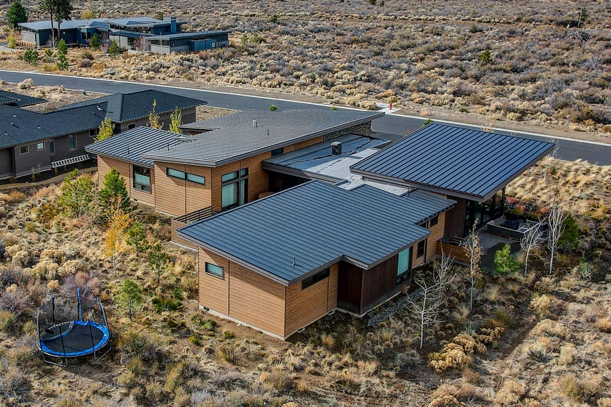 Modern house plan exterior with wood siding, flat roofs, and large windows set in a dry, arid landscape.