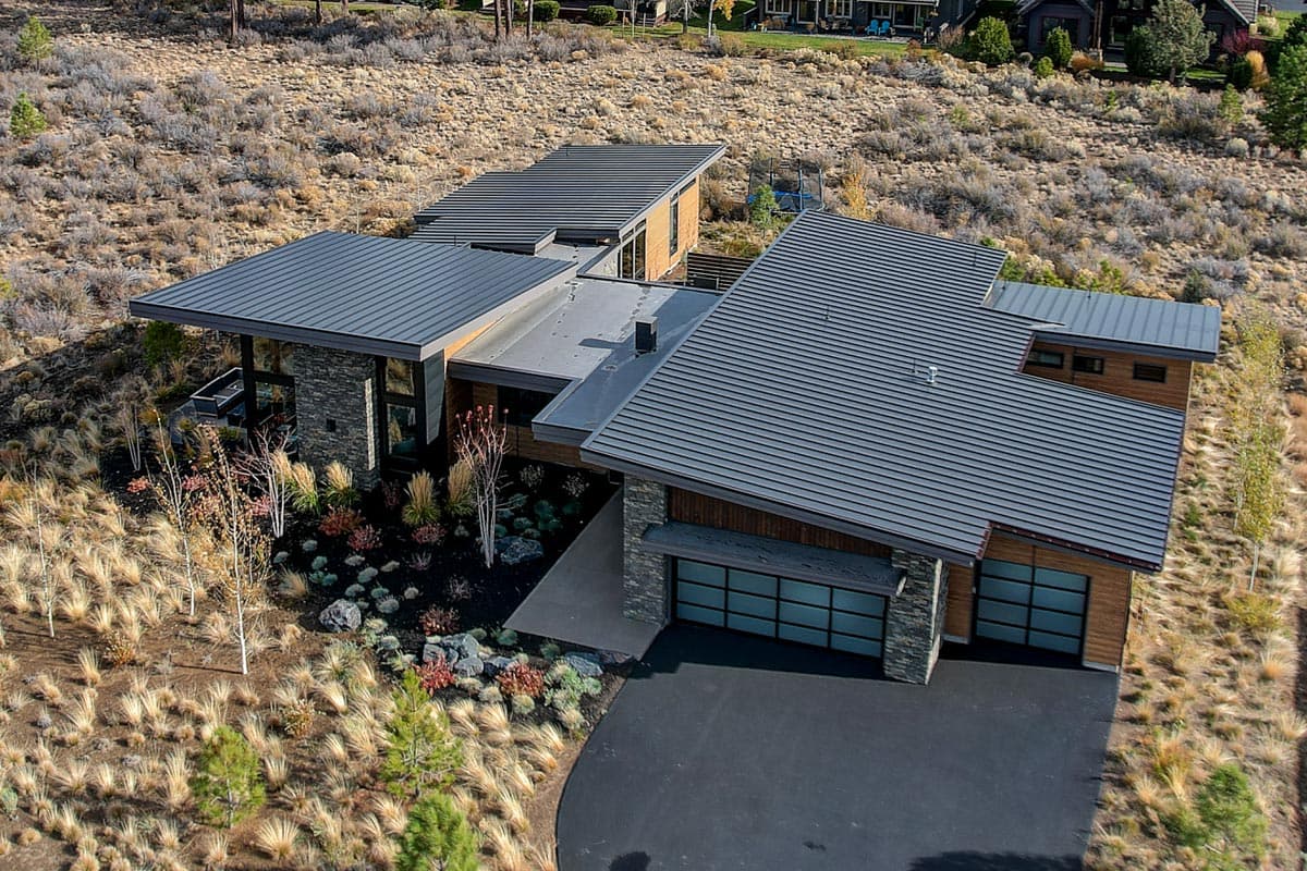 Modern house plan exterior with metal roof, stone accents, wood paneling, and a triple-car garage with frosted glass doors.