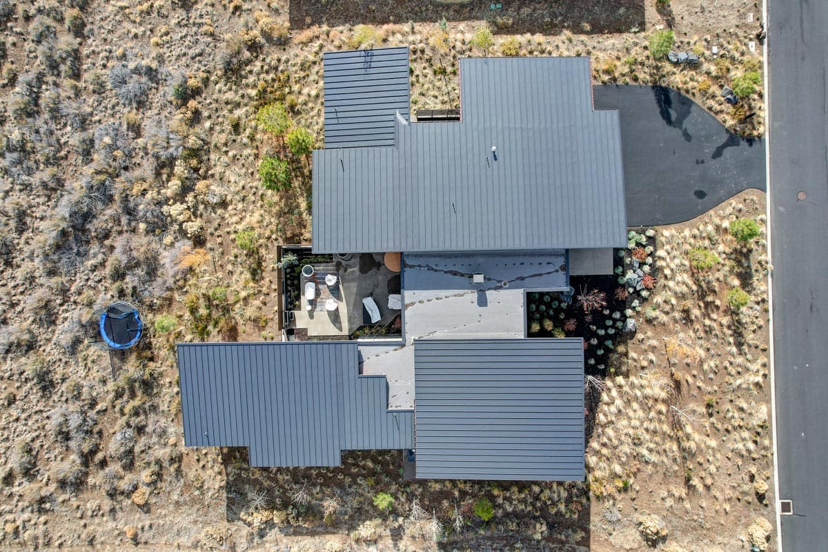 Modern house plan exterior with dark metal roof, courtyard, and surrounding dry landscape.