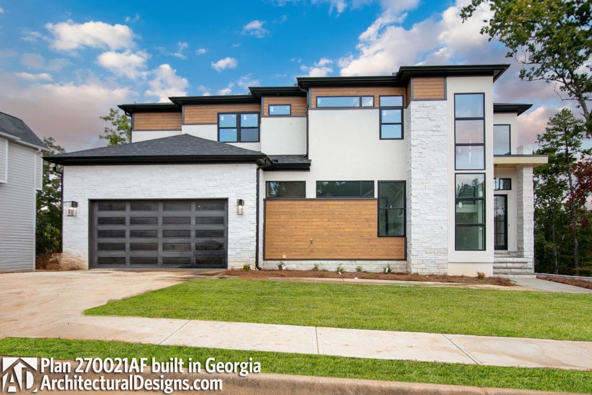 Modern house plan exterior with white stone, wood siding, layered rooflines, and a glass garage door.