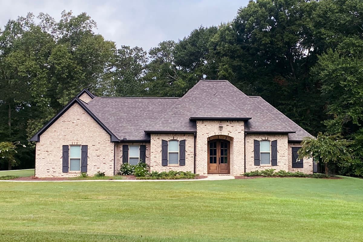 House plan exterior. One-story house with brick facade, gable roof, arched entryway, and multiple shuttered windows.
