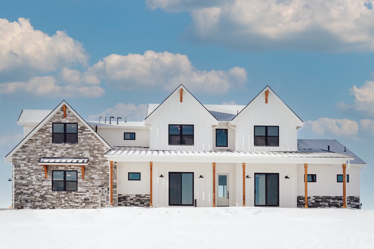 Modern Farmhouse house plan exterior with stone and white siding, multiple gables, covered porch, and dark-framed windows.