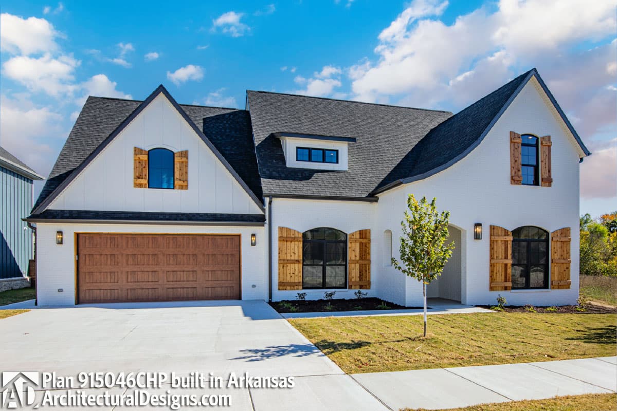 House plan exterior: Modern Farmhouse style, two stories, white brick, wood garage door, dormer, and gables with arched windows.