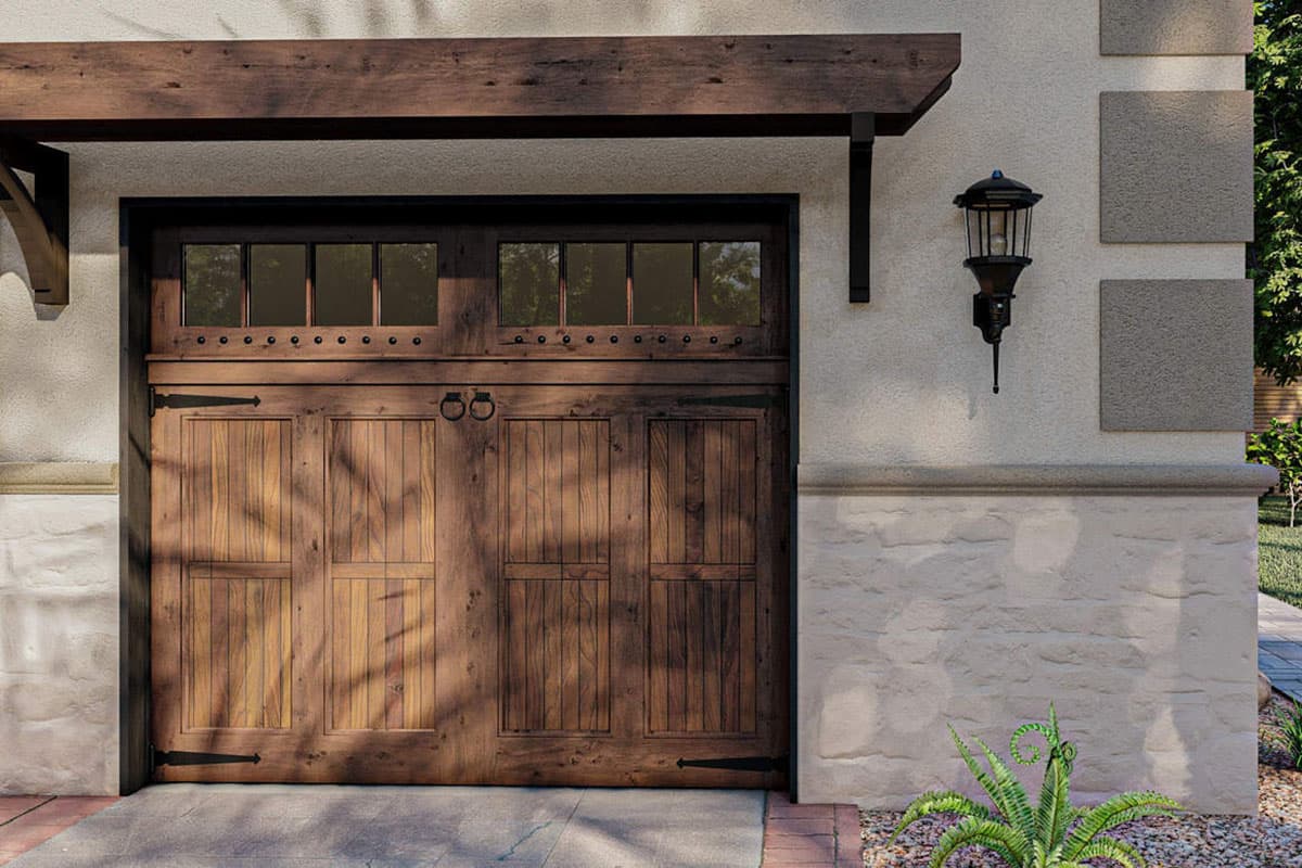 Wooden carriage house garage door with glass panes above, dark hardware, and timber beam pergola.