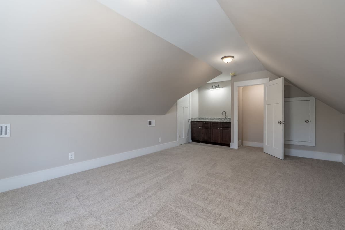 Attic room with sloped ceilings, a wet bar with dark cabinets, and an open doorway to storage.
