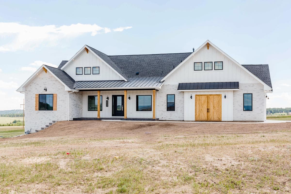 House plan exterior. Modern Farmhouse style, one-story. Features include gabled rooflines, porch with wooden supports, and brick facade.