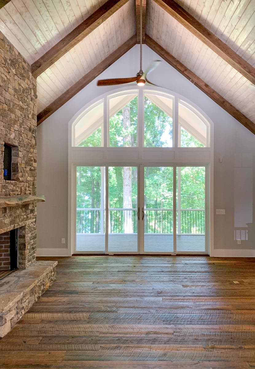 Great room with stone fireplace, vaulted beamed ceiling, and large arched window wall with sliding glass doors.