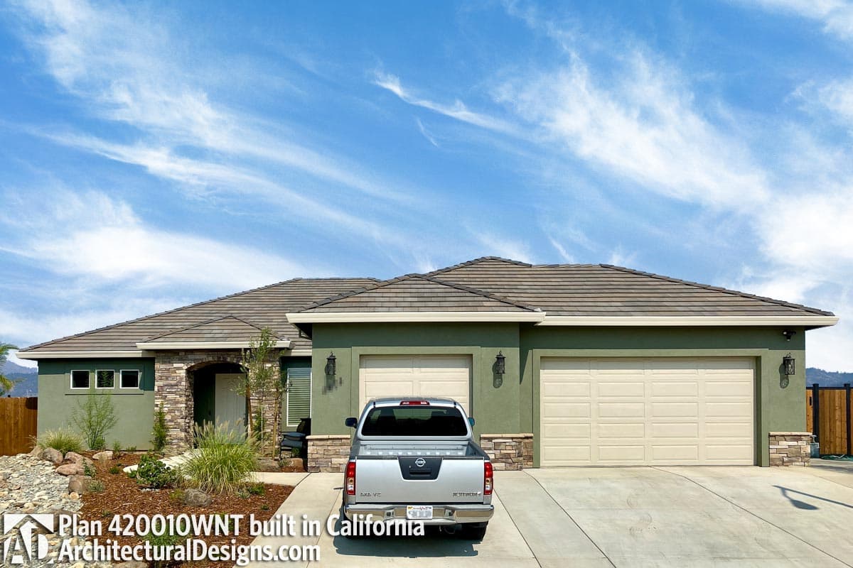 Single-story house plan exterior with arched stone entryway, three-window cluster, and attached two-car garage.