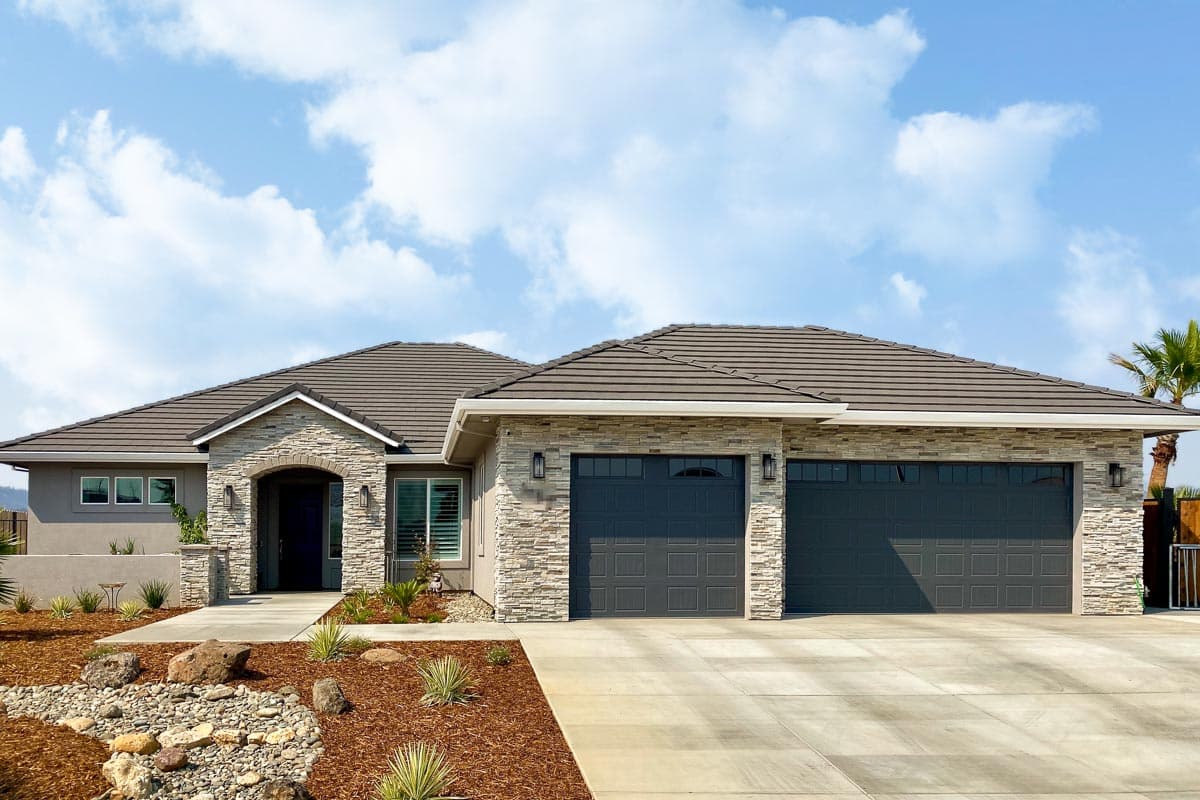 House plan exterior with a single story, stone facade, and a two-car garage. Features include an arched entryway and gabled rooflines.