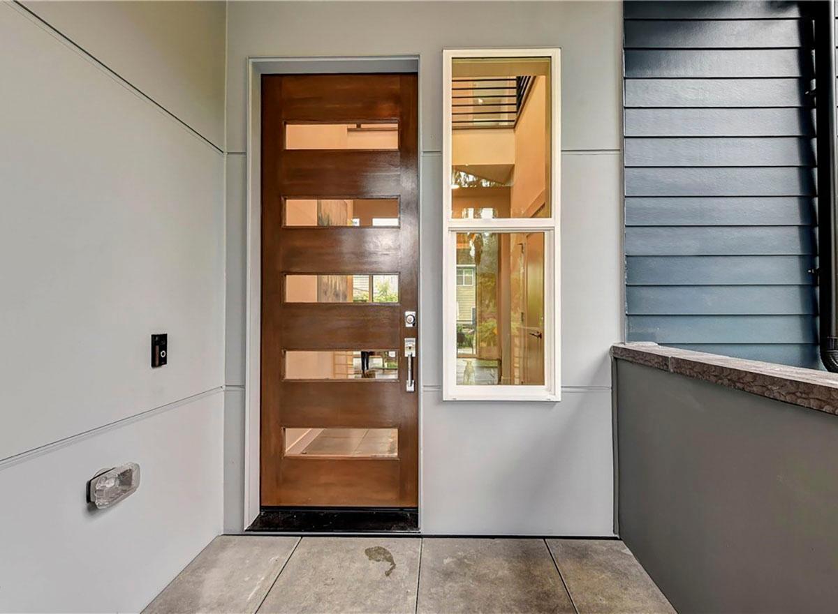 Modern house exterior with a wood door featuring horizontal glass panels and a tall, narrow window.