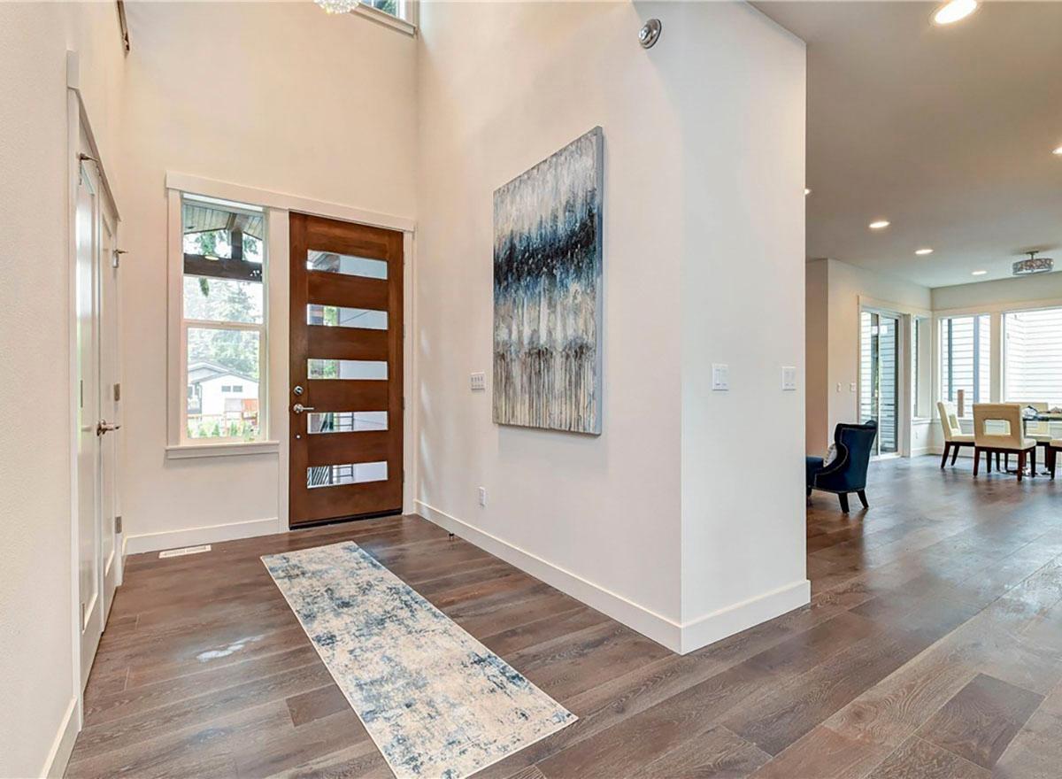 Interior view of entryway with modern wood door, side window, vaulted ceiling, and adjacent dining area with large windows.