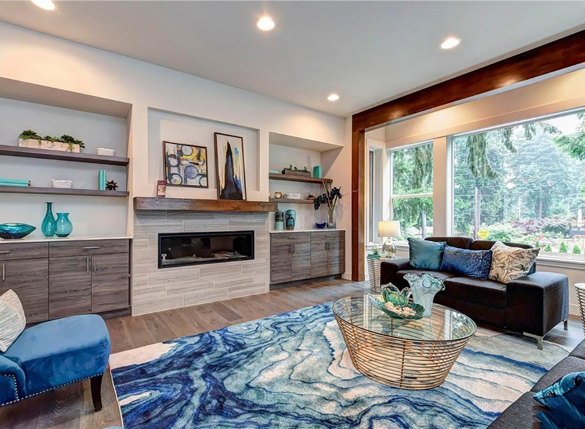 Living room with linear fireplace, built-in shelving, wood beam accent, and large picture windows.