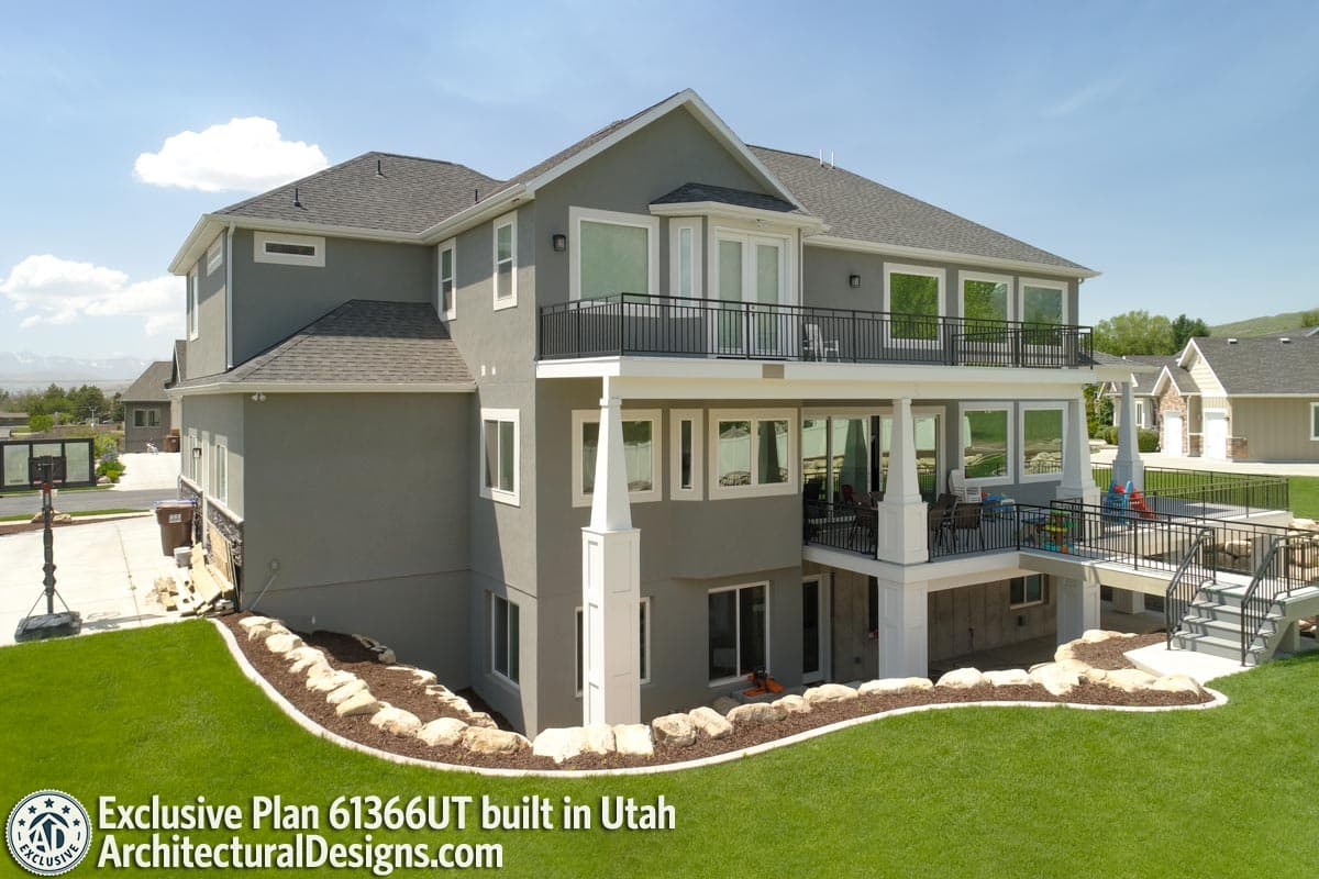 House plan exterior, two stories, gray stucco, large second-story balcony, covered lower-level patio with columns.