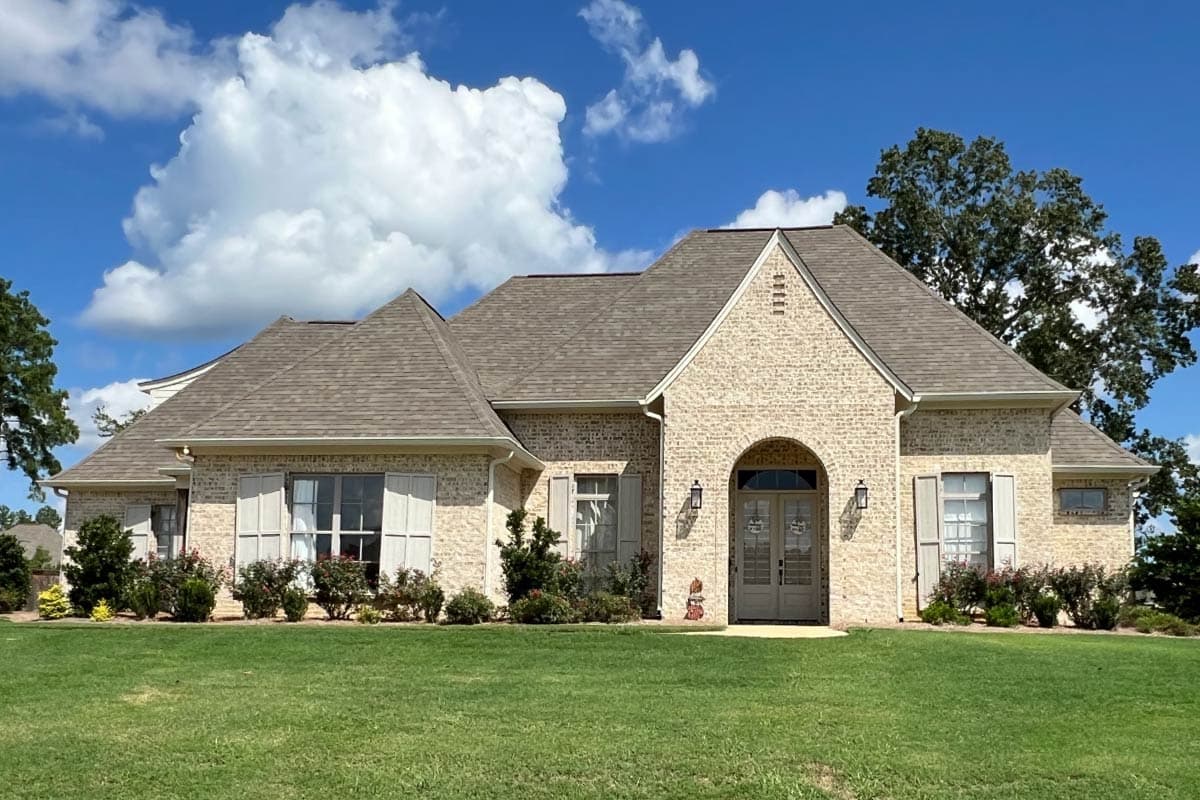 House plan exterior: One-story brick home with arched entry, gabled rooflines, and decorative shutters.