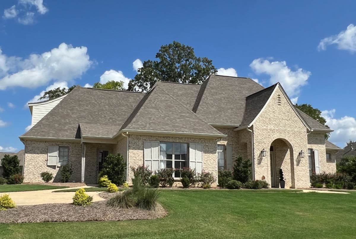 House plan exterior: One-story brick home with a prominent arched entry, varied rooflines, dormers, and louvered shutters.