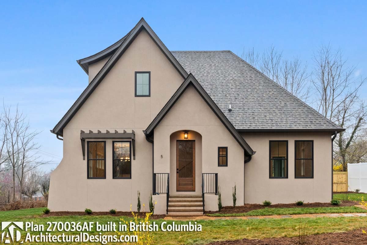 House plan exterior, stucco finish, prominent gables, arched entry with wooden door, dark-framed windows, and a steeply pitched roof.