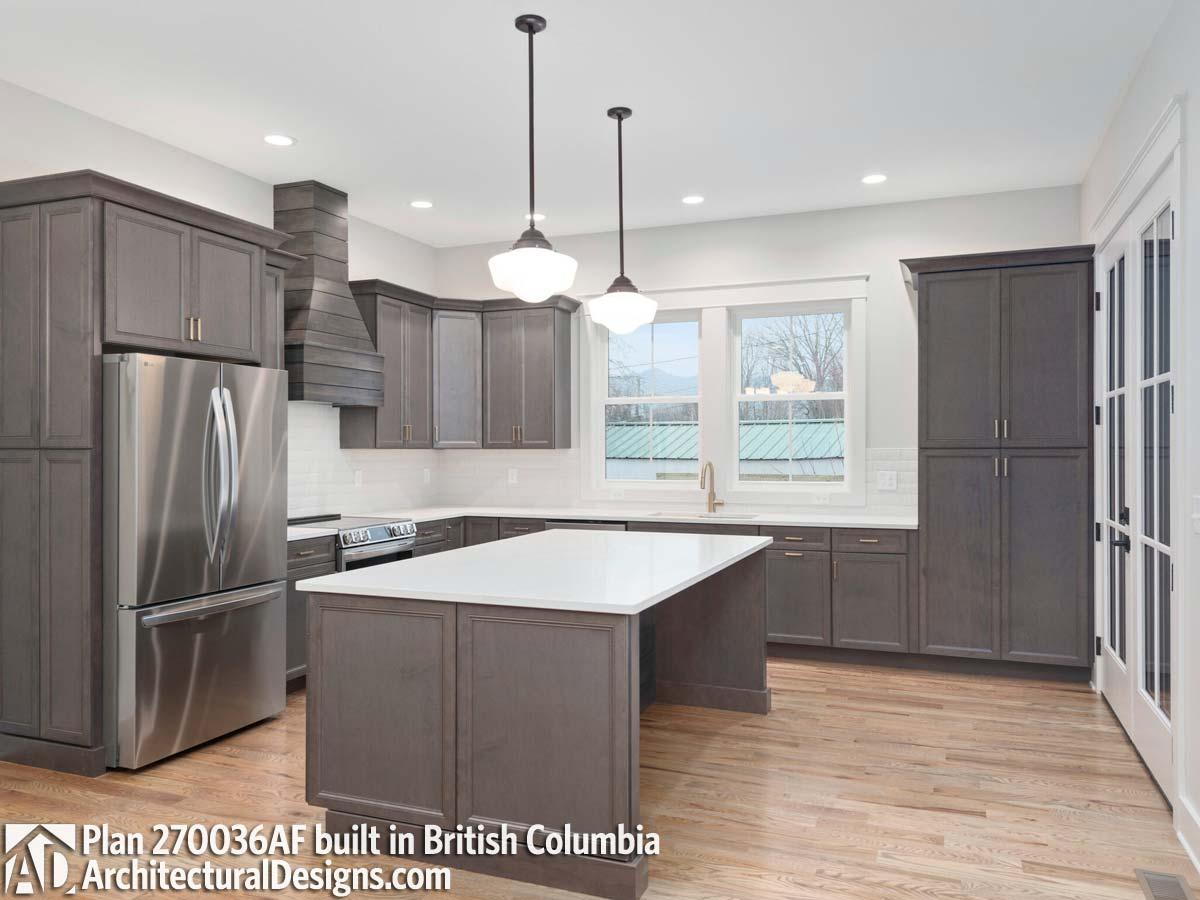Kitchen with gray cabinets, stainless steel appliances, island with white countertop, and white subway tile backsplash.